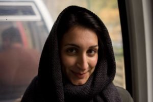 A young woman in a headscarf smiling, photographed through a car window