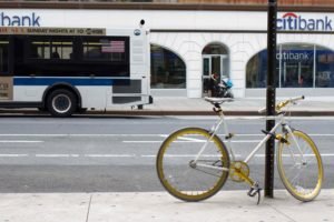 A bicycle locked to a post on a city street as a bus passes