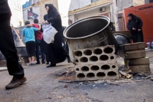 A large cooking pot and stacked blocks left in a street as people pass