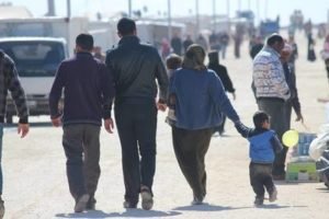 A family walking away across open ground, a child carrying a balloon