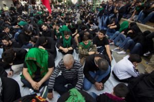 A crowd seated on the ground at an outdoor gathering, many of them wearing green