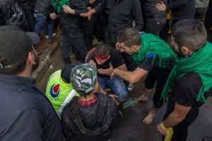 A young boy in a green mask among men wearing green headbands
